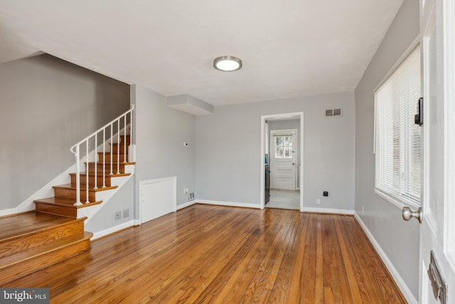 spare room featuring visible vents, baseboards, stairway, and hardwood / wood-style flooring