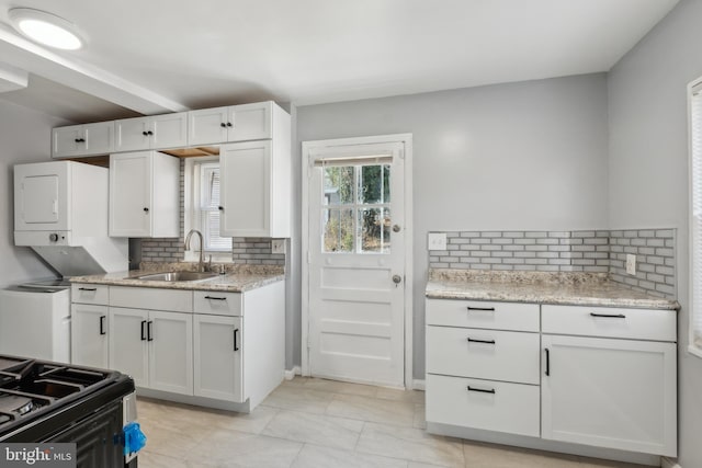 kitchen with a sink, decorative backsplash, white cabinets, and stacked washer / dryer