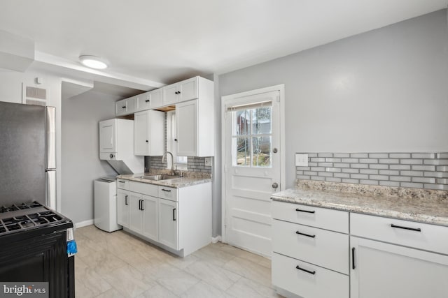 kitchen featuring white cabinets, stacked washer and clothes dryer, freestanding refrigerator, and a sink