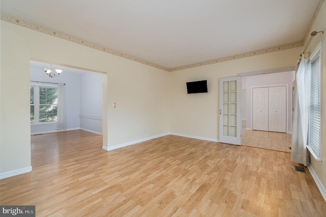 empty room with a notable chandelier, visible vents, baseboards, and light wood finished floors