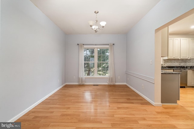 unfurnished dining area with baseboards, a notable chandelier, and light wood finished floors