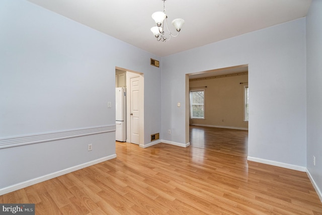 unfurnished room with light wood-style flooring, baseboards, visible vents, and a chandelier