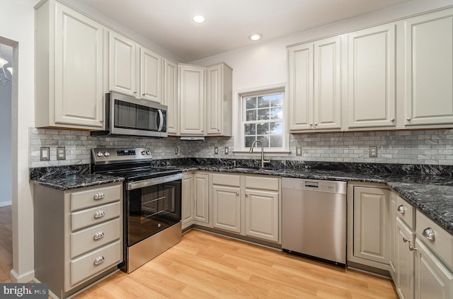 kitchen with dark stone countertops, light wood-style flooring, appliances with stainless steel finishes, and a sink