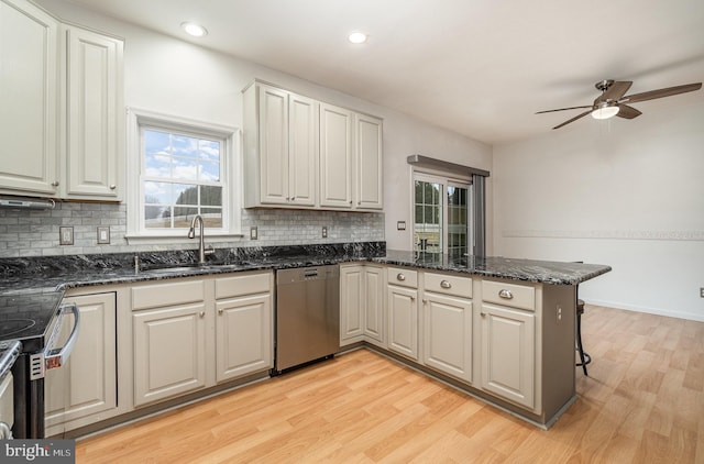 kitchen featuring light wood finished floors, ceiling fan, dishwasher, a peninsula, and a sink