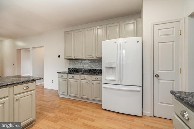 kitchen featuring light wood finished floors, backsplash, white refrigerator with ice dispenser, and dark stone counters