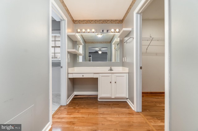 bathroom featuring a spacious closet, vanity, baseboards, and wood finished floors