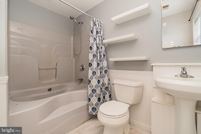 bathroom with toilet, marble finish floor, shower / tub combo with curtain, and wainscoting