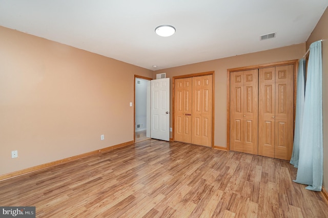 unfurnished bedroom with light wood-style floors, baseboards, two closets, and visible vents