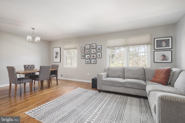 living area with a notable chandelier, light wood-style flooring, visible vents, and baseboards