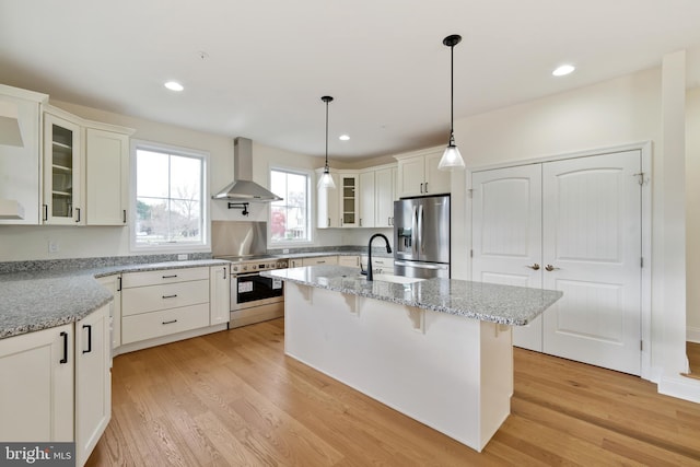 kitchen with stainless steel appliances, light wood-style floors, white cabinetry, wall chimney exhaust hood, and a sink