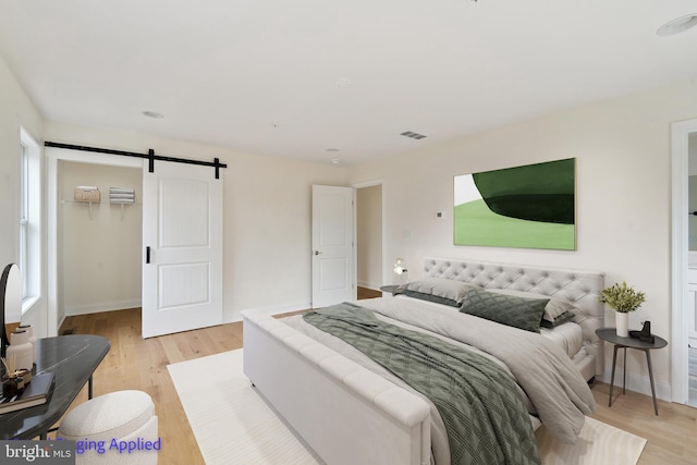 bedroom featuring a walk in closet, a barn door, baseboards, and light wood finished floors