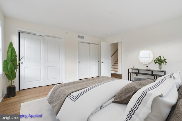 bedroom with visible vents, two closets, and wood finished floors