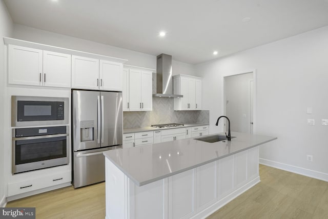 kitchen with a sink, light wood-style floors, appliances with stainless steel finishes, white cabinetry, and wall chimney exhaust hood