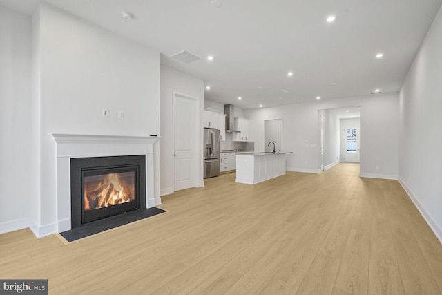 unfurnished living room featuring recessed lighting, light wood-type flooring, a fireplace with flush hearth, and visible vents