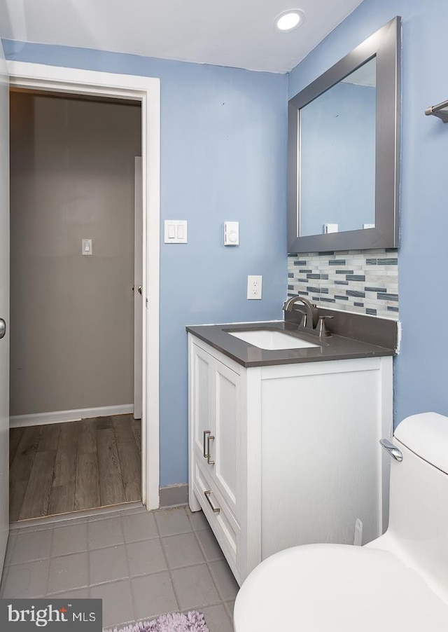 bathroom featuring vanity, toilet, baseboards, and backsplash