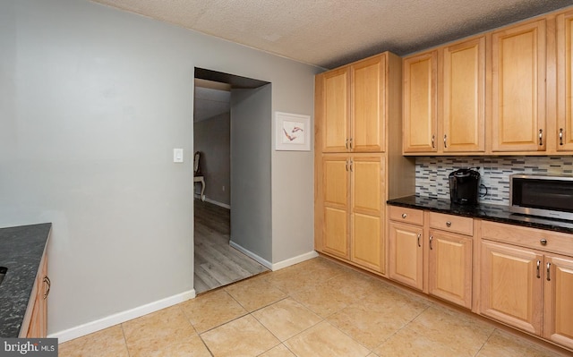 kitchen featuring baseboards, light tile patterned flooring, a textured ceiling, stainless steel microwave, and tasteful backsplash