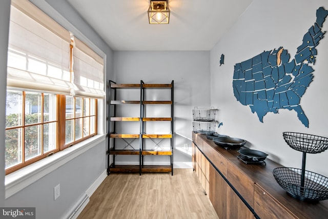 interior space with a baseboard heating unit, baseboards, and light wood-style flooring