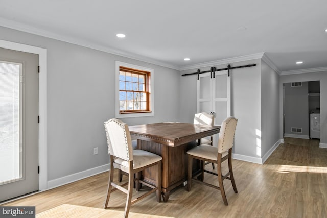 dining space featuring a barn door, ornamental molding, visible vents, and washer / dryer