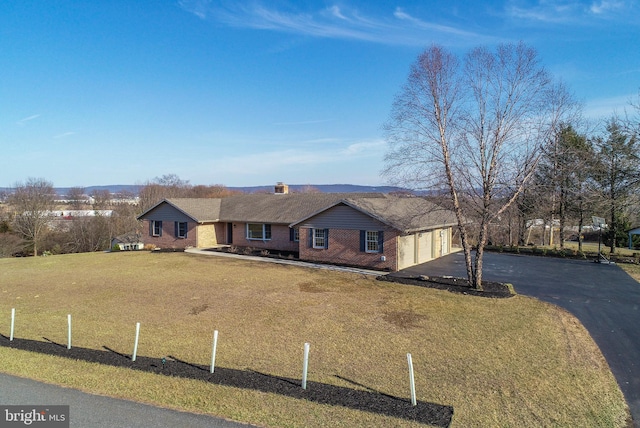 ranch-style house with a front yard, a chimney, a garage, aphalt driveway, and brick siding