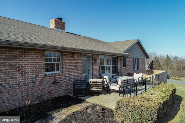 back of house with roof with shingles, an outdoor hangout area, brick siding, a chimney, and a patio area