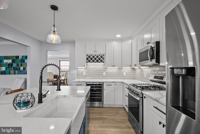 kitchen featuring beverage cooler, a sink, stainless steel appliances, light wood-style floors, and decorative light fixtures