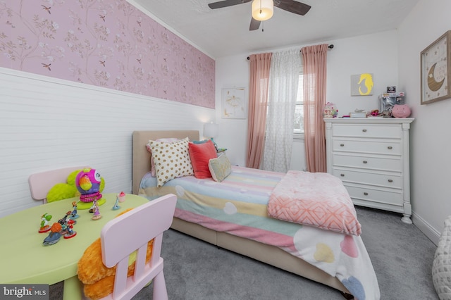 carpeted bedroom with a wainscoted wall, ceiling fan, and wallpapered walls