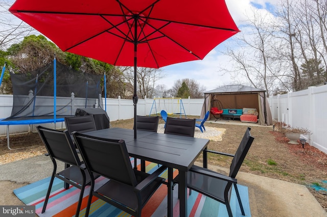 view of patio with a fenced backyard, a trampoline, and outdoor dining space