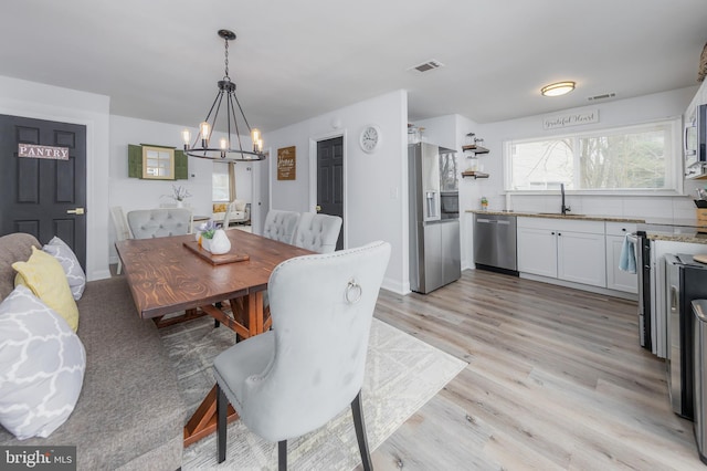 dining area with visible vents, a notable chandelier, and light wood-style flooring