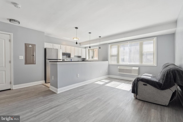 interior space featuring electric panel, light wood-style floors, baseboards, and a wall mounted AC