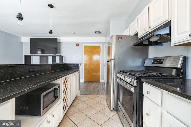 kitchen with light tile patterned floors, dark stone counters, white cabinets, under cabinet range hood, and stainless steel gas stove