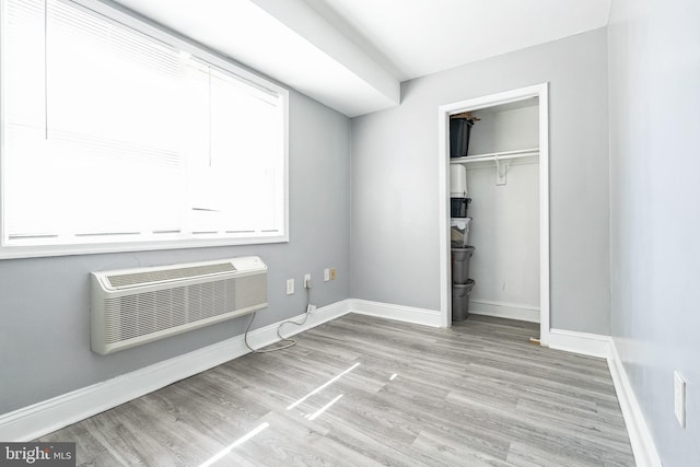 unfurnished bedroom with a closet, baseboards, wood finished floors, and a wall mounted AC