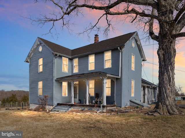 view of front of home with a front lawn, covered porch, a chimney, and fence