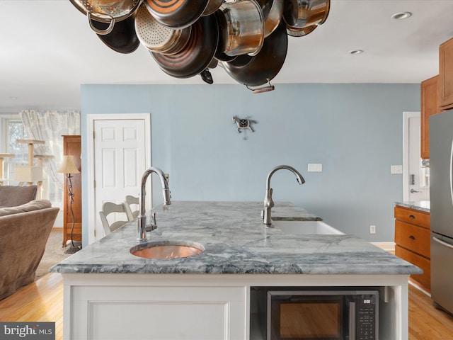 kitchen with a sink, light stone counters, a center island with sink, and freestanding refrigerator