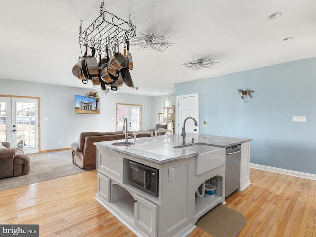 kitchen with a kitchen island with sink, a sink, open floor plan, built in microwave, and dishwasher