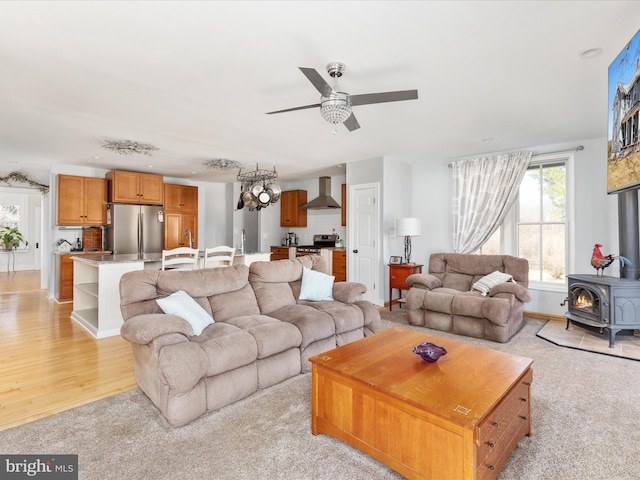 living room featuring a wood stove, a ceiling fan, and light wood finished floors