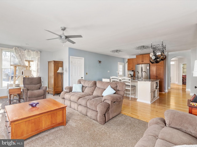 living room with arched walkways, a healthy amount of sunlight, ceiling fan, and light wood finished floors