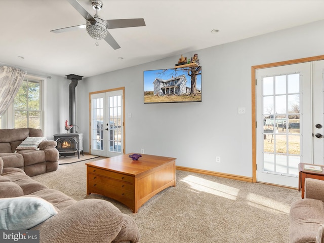 living area with carpet, baseboards, a wood stove, ceiling fan, and french doors