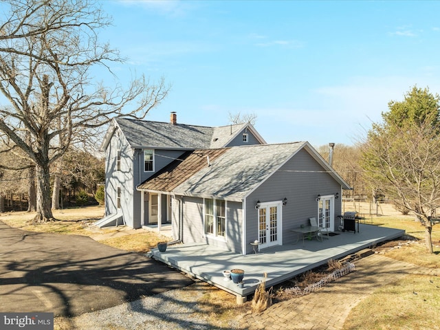 rear view of house with a chimney, french doors, a wooden deck, and a shingled roof