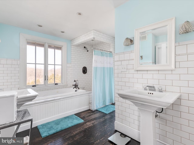 full bath featuring a tub, wood finished floors, tile walls, wainscoting, and tiled shower