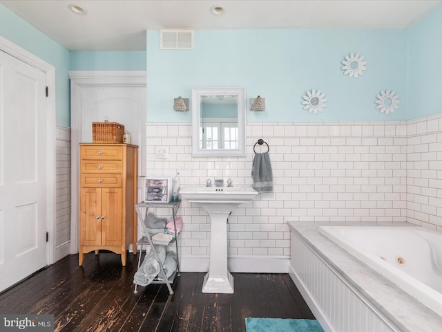 full bathroom with hardwood / wood-style flooring, a tub with jets, visible vents, and wainscoting