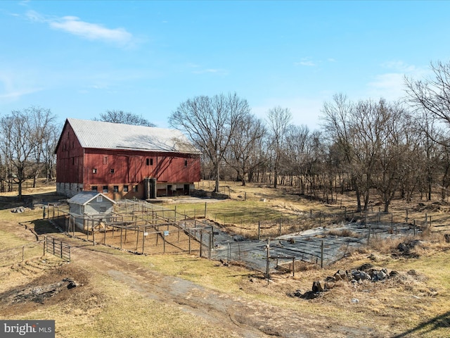 view of yard featuring a rural view, a barn, fence, and an outbuilding