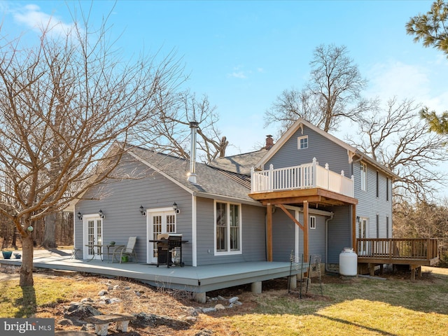 back of house with a wooden deck, roof with shingles, french doors, a chimney, and a yard