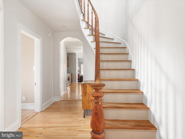 staircase with wood finished floors, arched walkways, and baseboards