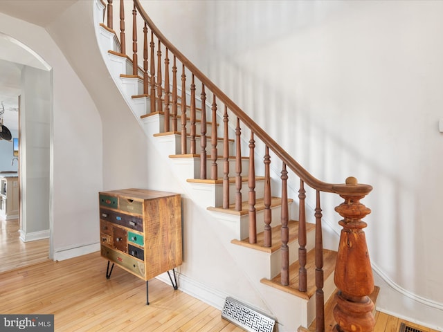 staircase with visible vents, arched walkways, baseboards, and hardwood / wood-style floors