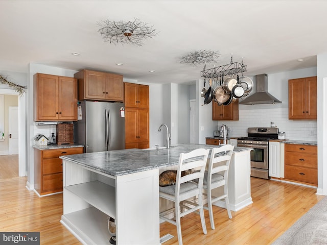 kitchen featuring open shelves, a sink, wall chimney range hood, stainless steel appliances, and light wood finished floors