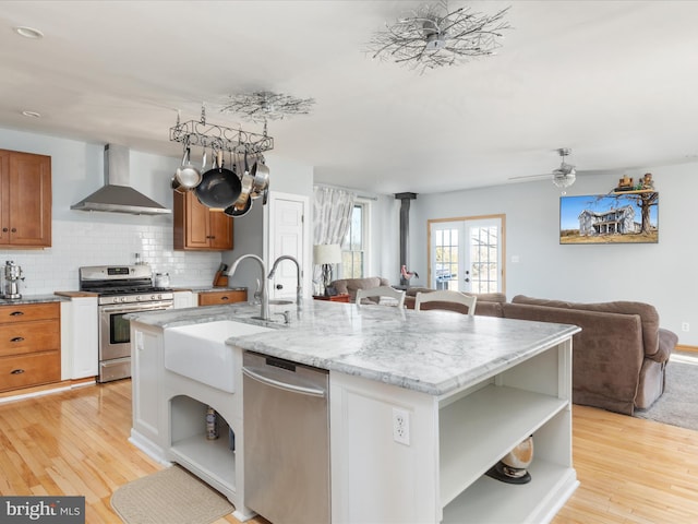 kitchen with open shelves, a sink, open floor plan, appliances with stainless steel finishes, and wall chimney exhaust hood