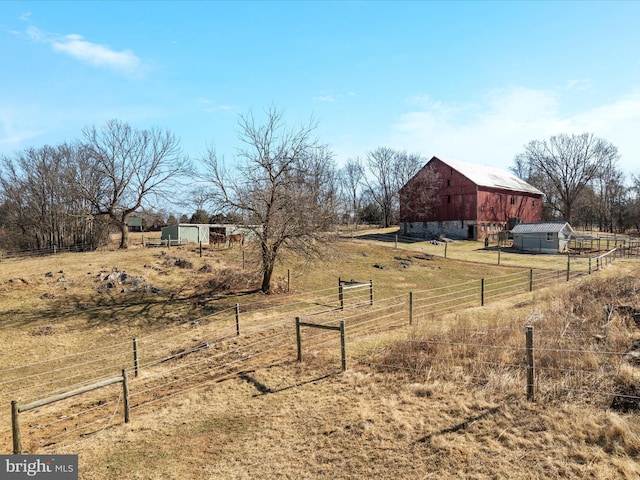 view of yard with an outbuilding, a rural view, a barn, and fence