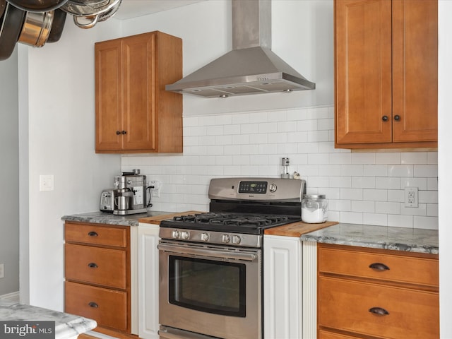 kitchen featuring brown cabinetry, wall chimney range hood, stainless steel range with gas stovetop, and tasteful backsplash