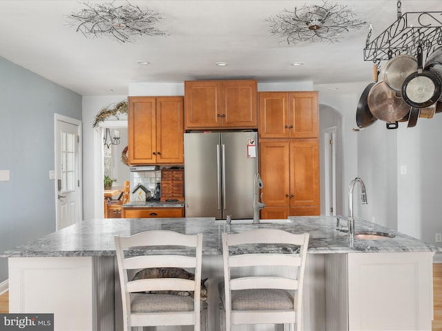 kitchen featuring an island with sink, a sink, tasteful backsplash, freestanding refrigerator, and arched walkways