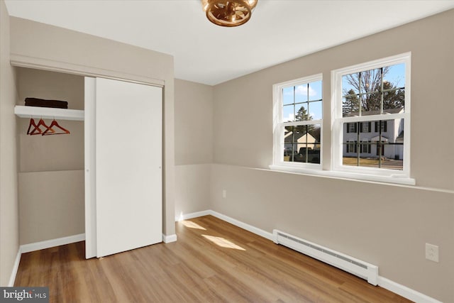 unfurnished bedroom with baseboards, wood finished floors, a closet, and a baseboard radiator